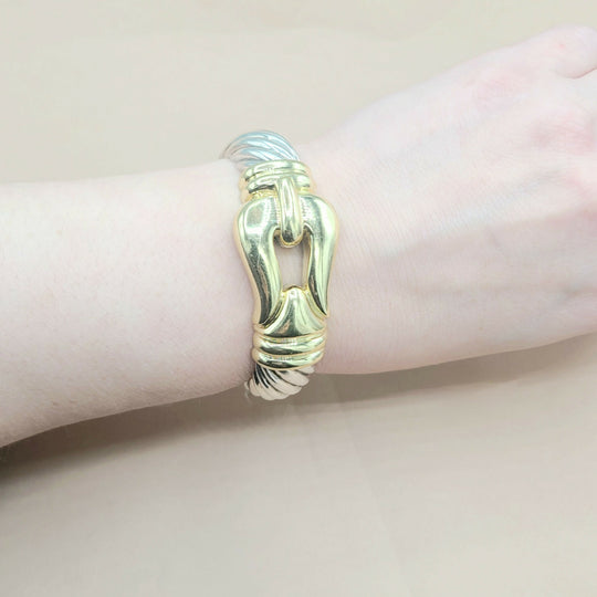 Gold bracelet on a wrist against a neutral background