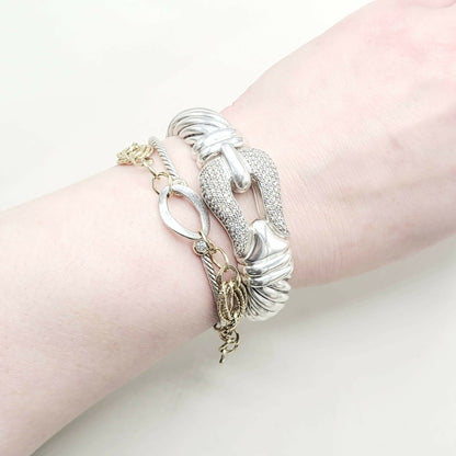 Wrist wearing multiple silver and gold bracelets on a light background