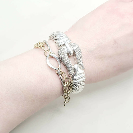 Wrist wearing multiple silver and gold bracelets on a light background