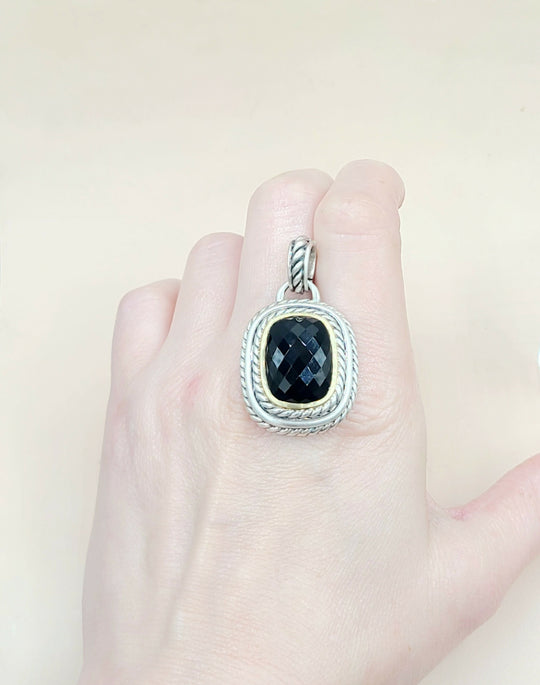 Silver pendant with a black stone on a hand against a light background