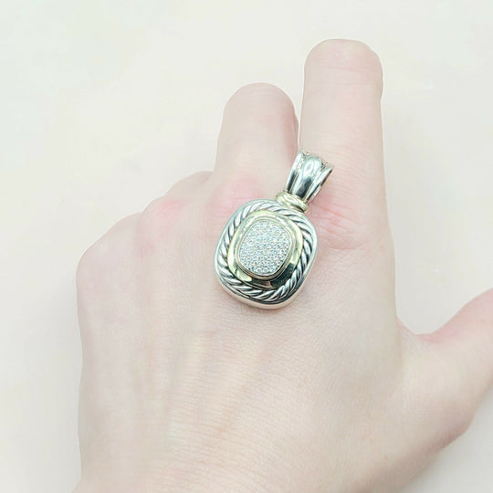 Silver pendant on a finger against a plain background