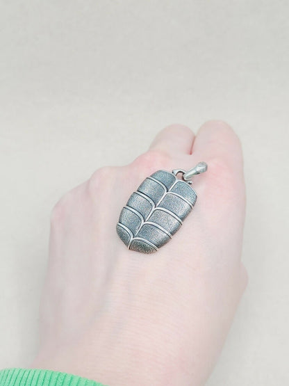 Hand holding a silver pendant against a plain background