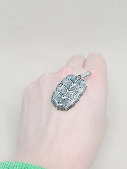 Hand holding a silver pendant against a plain background
