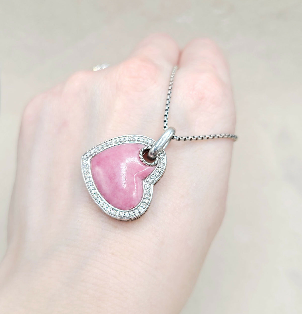 Pink heart-shaped pendant on a silver chain held in a hand against a light background