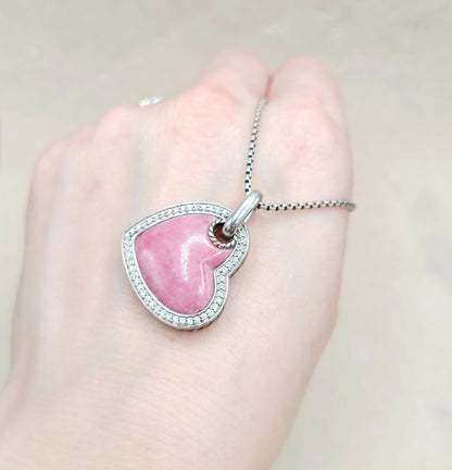 Pink heart-shaped pendant on a silver chain held in a hand against a light background
