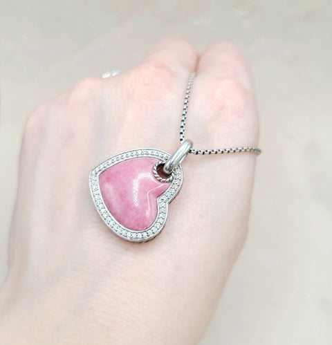 Pink heart-shaped pendant on a silver chain held in a hand against a light background