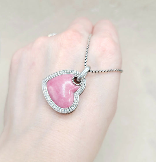 Pink heart-shaped pendant on a silver chain held in a hand against a light background