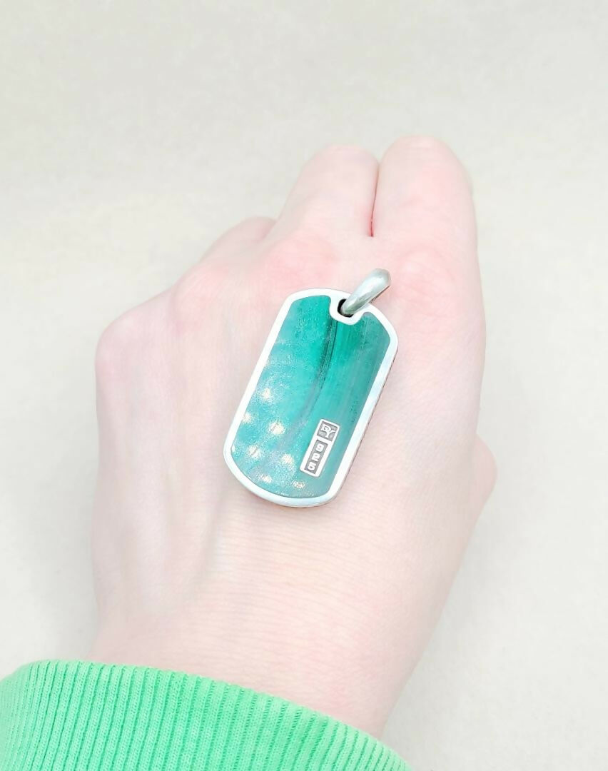 Hand holding a teal dog tag with a white background