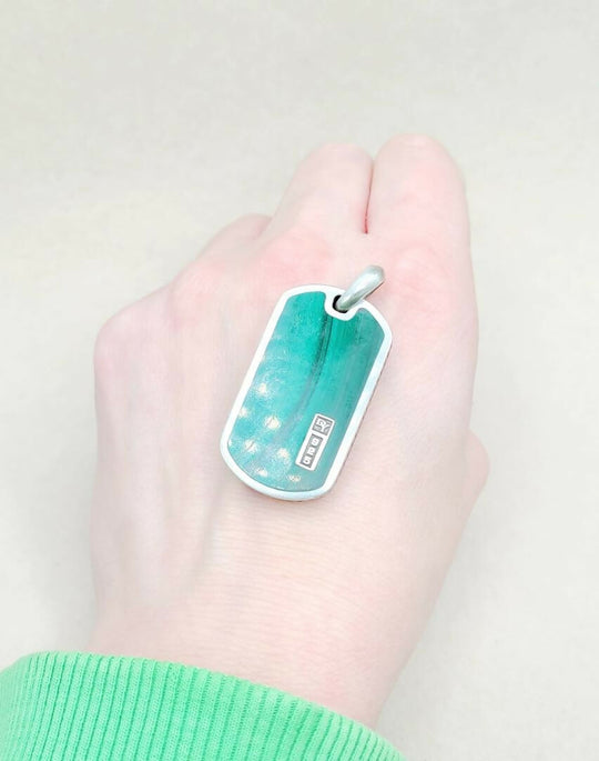 Hand holding a teal dog tag with a white background