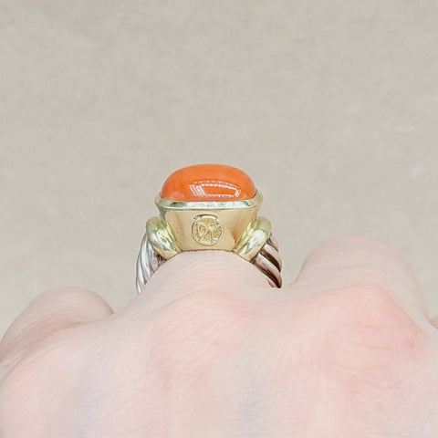 Gold ring with a coral stone on a finger against a neutral background