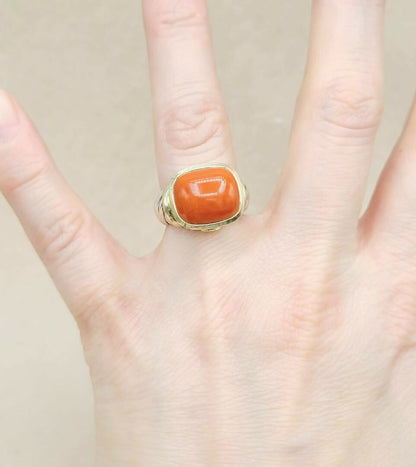 Gold ring with a red stone on a hand against a neutral background