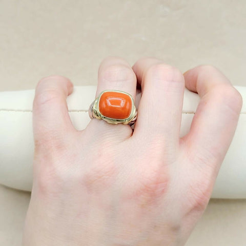Hand wearing a ring with a red stone on a neutral background