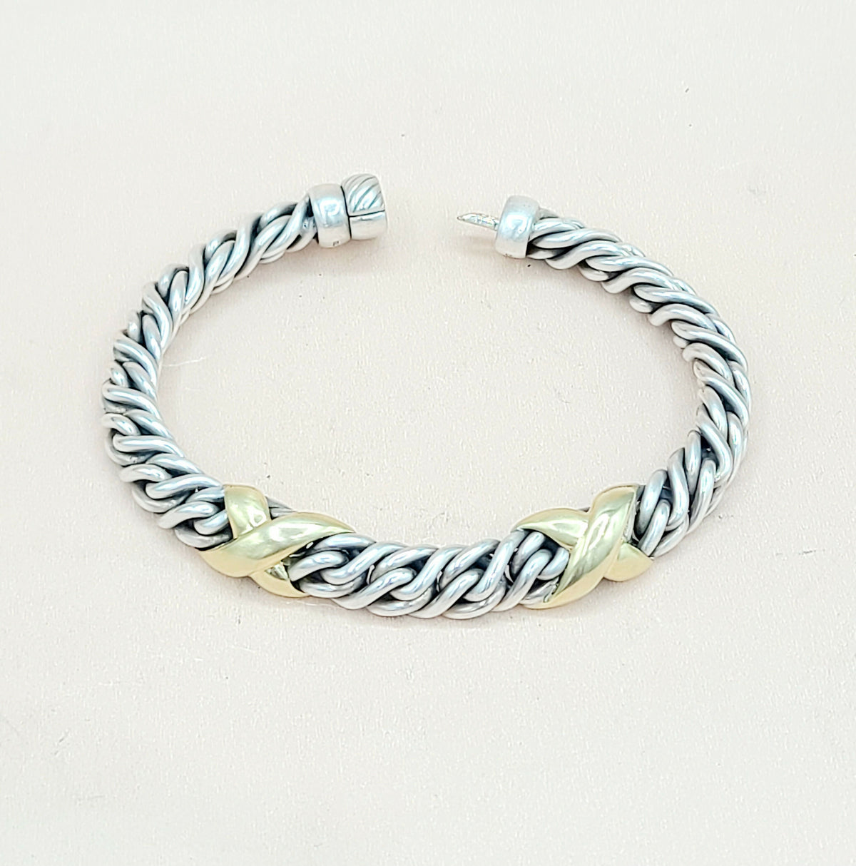 Silver and gold braided bracelet on a light beige background