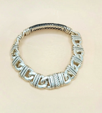 A sterling silver cable-knit bracelet with textured twisted links and a polished inner band, displayed on a light beige background.