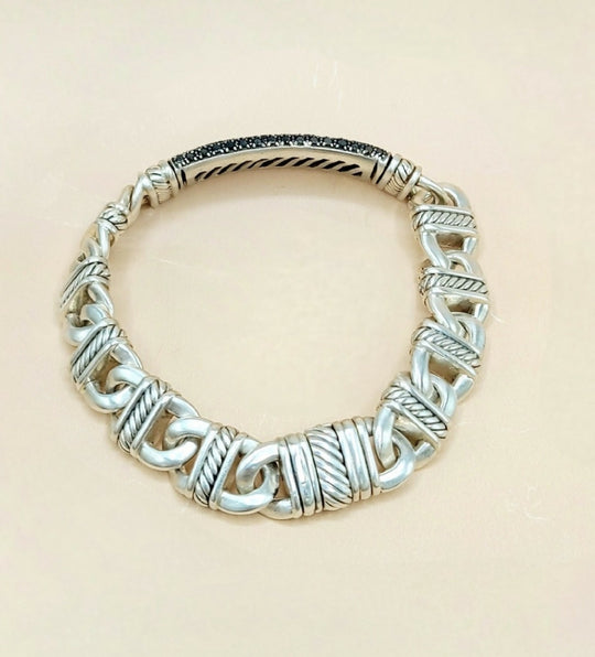 A sterling silver cable-knit bracelet with textured twisted links and a polished inner band, displayed on a light beige background.