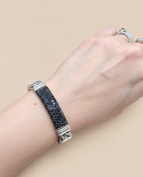 A sterling silver cuff bracelet with a textured, glittery black center panel, shown worn on a person's wrist against a solid beige background.