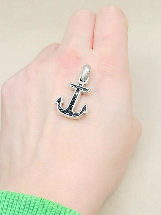 Silver anchor pendant on a hand against a plain background
