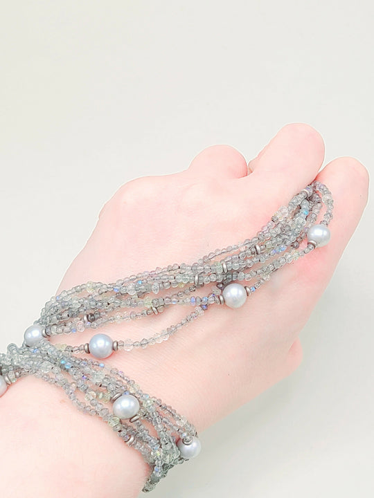 Hand wearing a multi-layered beaded bracelet on a light background