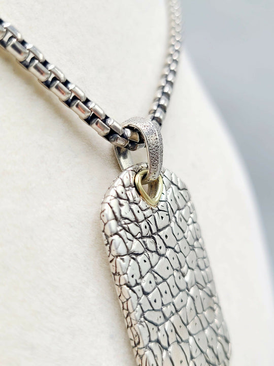 A silver textured dog tag pendant necklace with a box chain, displayed on a white jewelry bust.