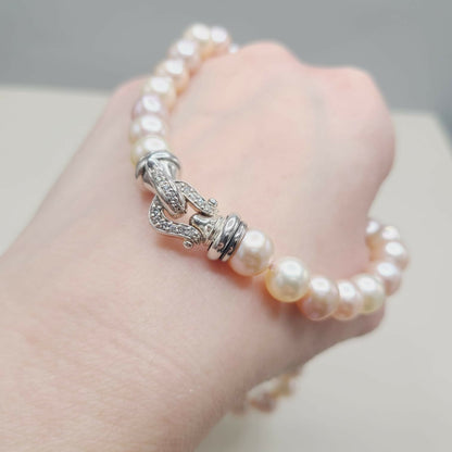 Pearl bracelet with silver clasp on a hand against a neutral background