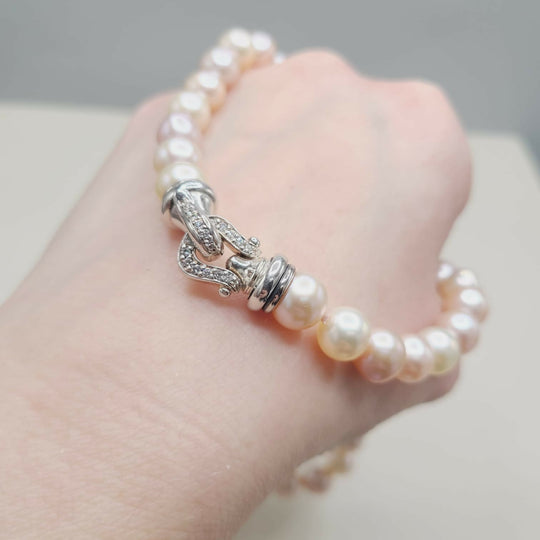 Pearl bracelet with silver clasp on a hand against a neutral background