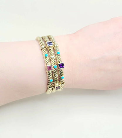 Gold bracelets with gemstones on a wrist against a white background
