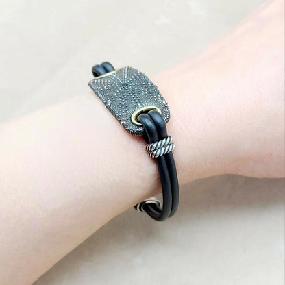 Black leather bracelet with textured metal clasp on a wrist against a neutral background