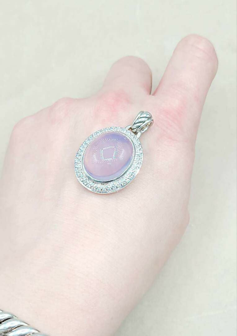Hand holding a silver pendant with a purple stone against a plain background