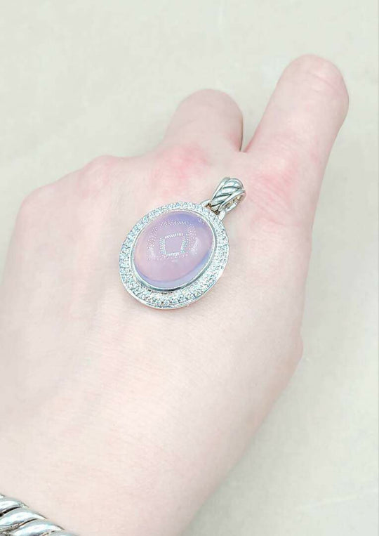 Hand holding a silver pendant with a purple stone against a plain background