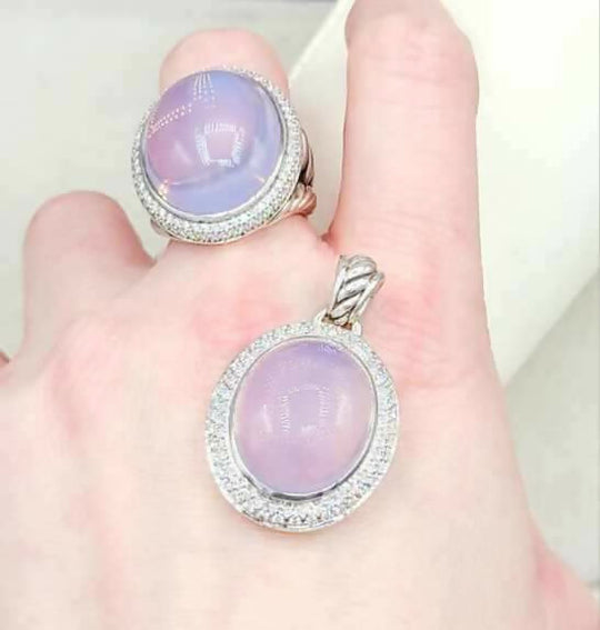 Ring and pendant with purple gemstones on a hand against a white background