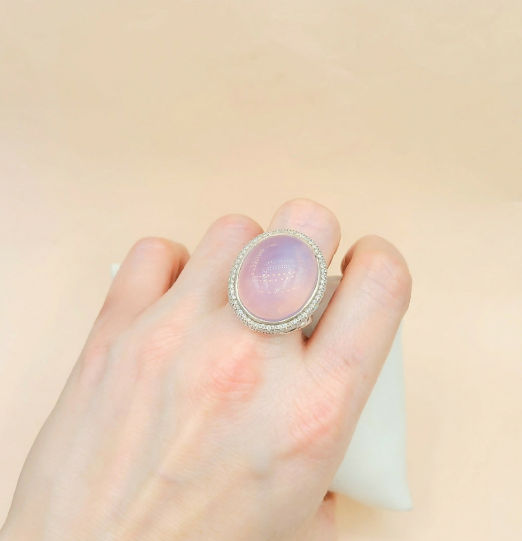 Hand wearing a ring with a pink stone on a beige background