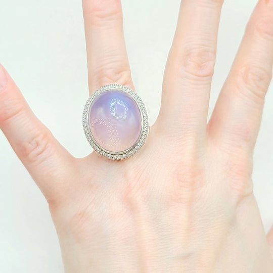 Hand wearing a ring with a colorful gemstone on a light background