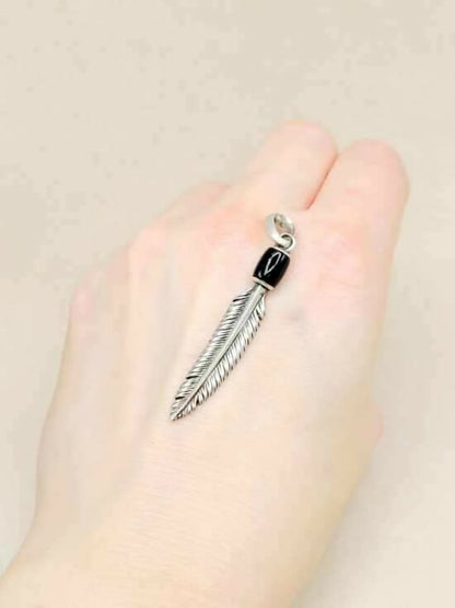 Feather-shaped earring on a hand against a beige background