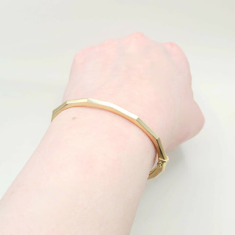 Gold bracelet on a wrist against a light gray background