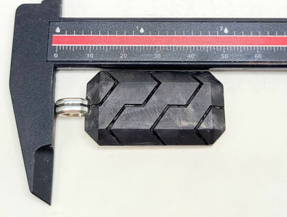 Black geometric object on a white background with a caliper for scale