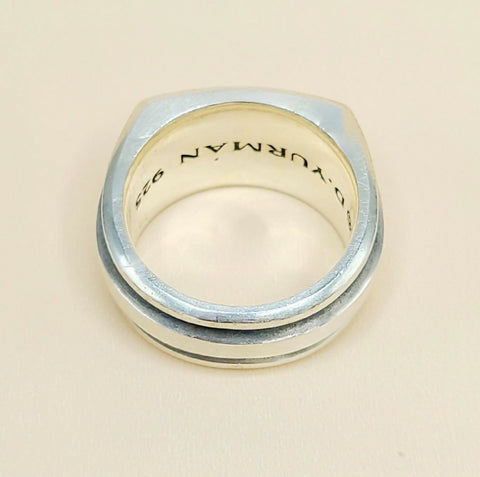 A silver-toned metal ring with a square-shaped face and a double beveled edge, featuring the engraved text 'D. YURMAN 925' inside, shown on a light beige background.