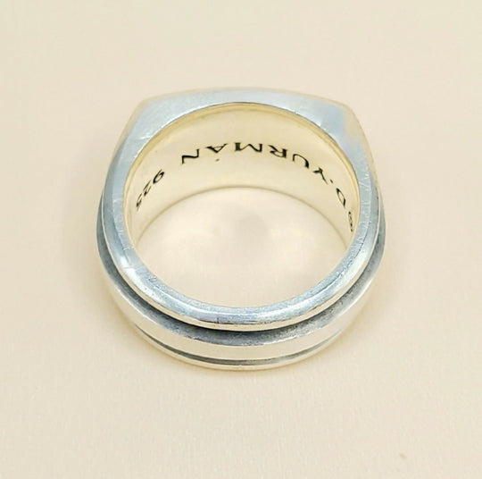 A silver-toned metal ring with a square-shaped face and a double beveled edge, featuring the engraved text 'D. YURMAN 925' inside, shown on a light beige background.