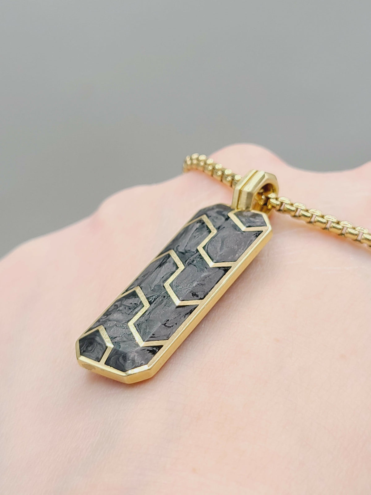Gold necklace with a geometric pendant on a hand against a gray background