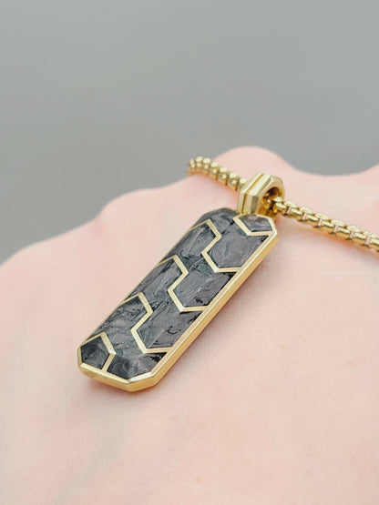 Gold necklace with a geometric pendant on a hand against a gray background