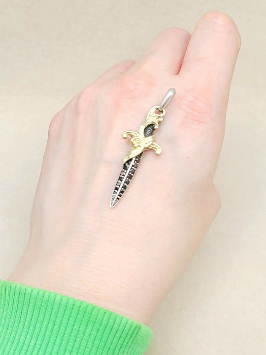 Hand wearing a green sleeve with a small dagger-shaped pendant on a beige background