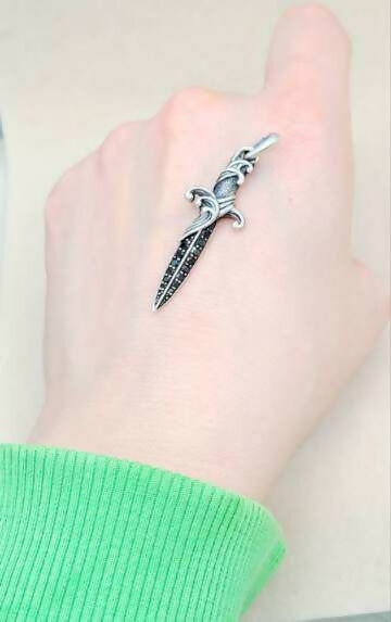Silver dagger-shaped ring on a person's finger with a light background