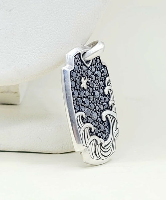 A sterling silver pendant featuring a wave design with a black pavé star motif in the center, displayed on a white jewelry stand.