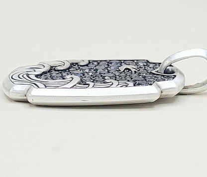 A sterling silver pendant with a textured dark inlay and engraved wave-like patterns, shown on a light gray background.