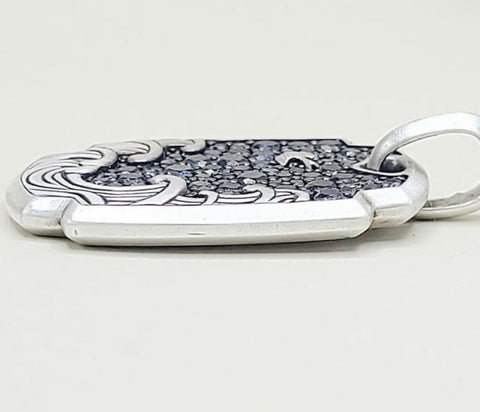 A sterling silver pendant with a textured dark inlay and engraved wave-like patterns, shown on a light gray background.