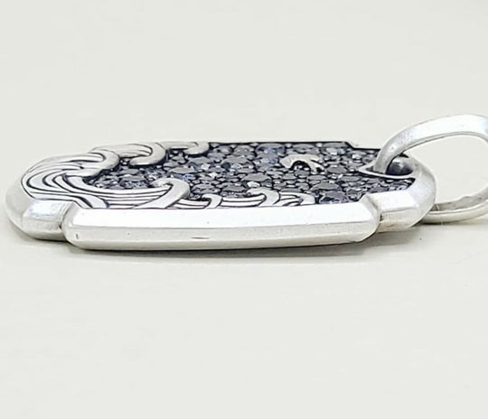 A sterling silver pendant with a textured dark inlay and engraved wave-like patterns, shown on a light gray background.