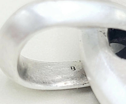 Close-up of a silver-toned ring with a small engraved letter 'B' on the inside band, photographed against a plain light background.