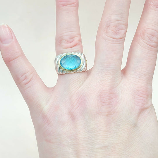 Hand wearing a ring with a blue gemstone on a plain background