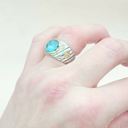 Hand wearing a ring with a blue gemstone on a light background