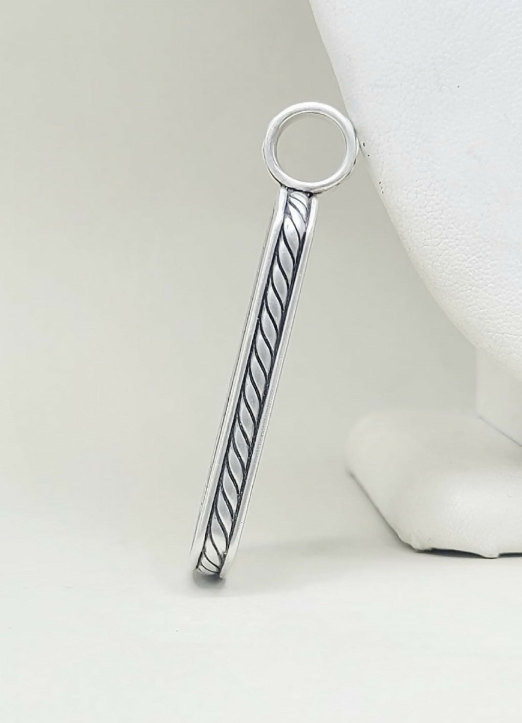 A sterling silver bar pendant with a twisted cable design and a circular loop at the top, displayed on a white jewelry bust against a light gray background.