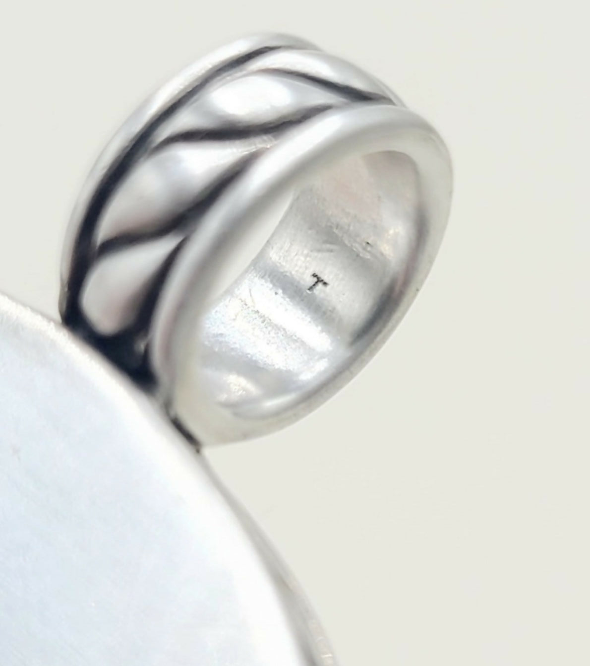 A close-up of a silver ring with a textured, wavy band design, resting on a plain light background.